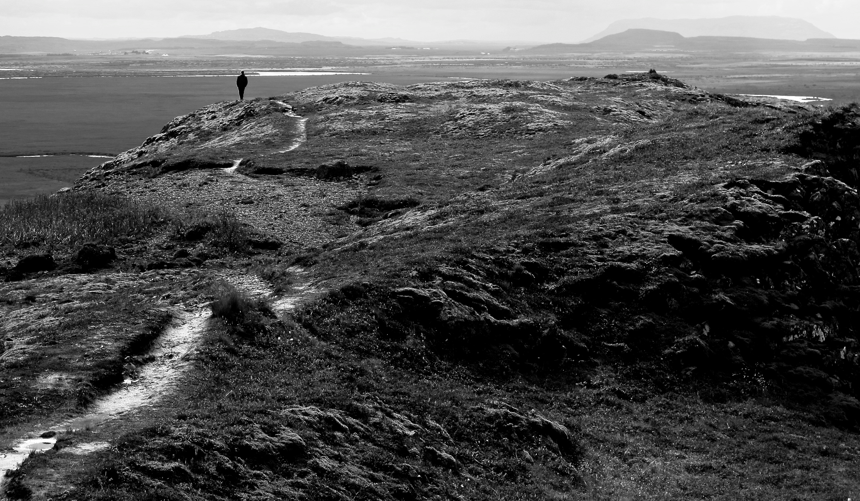 a black and white photo of a mountain path leading into the distance in iceland. There is a man standing far down the path.