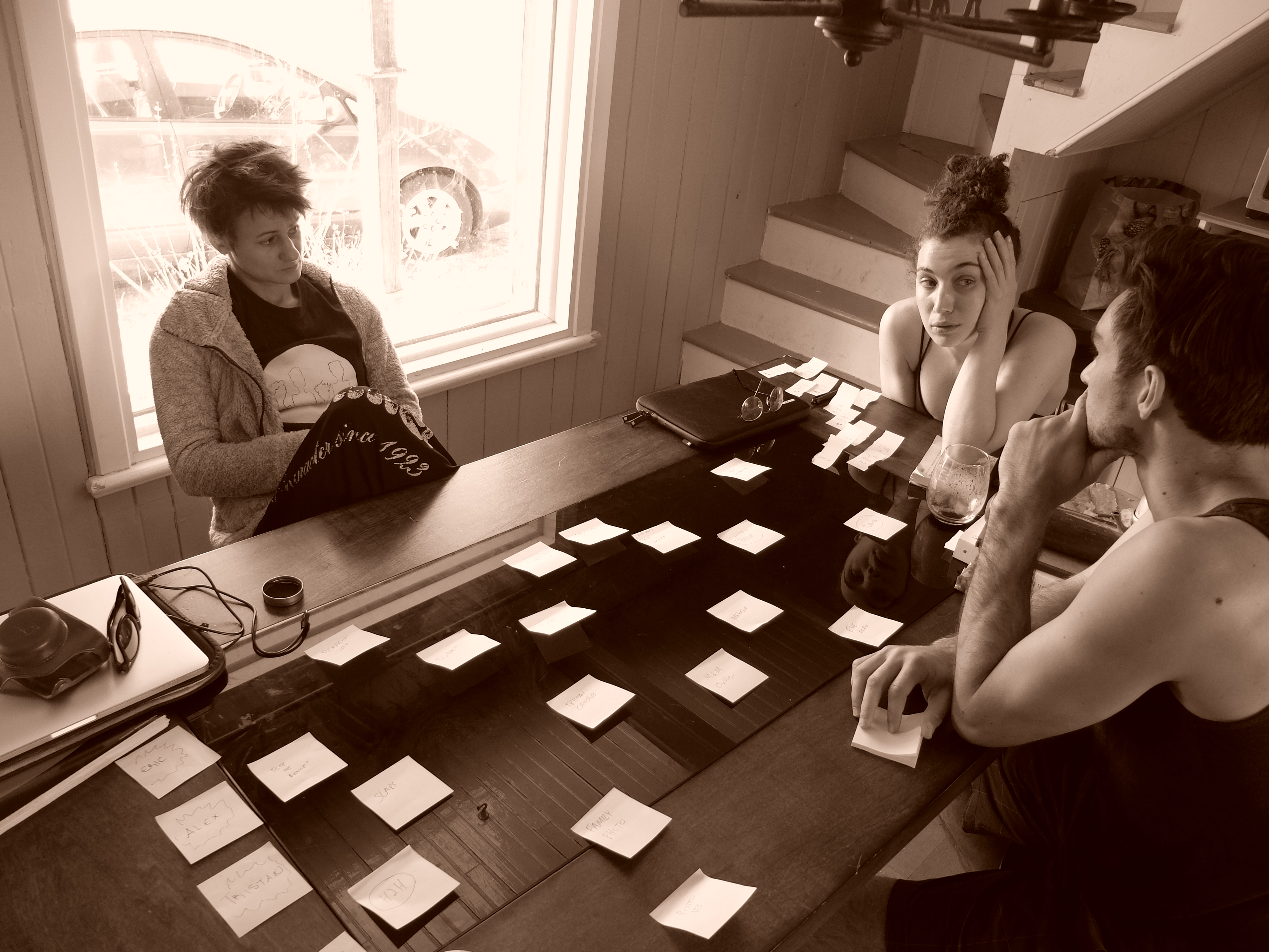 Three people sitting around a table of sticky notes discussing the creative process